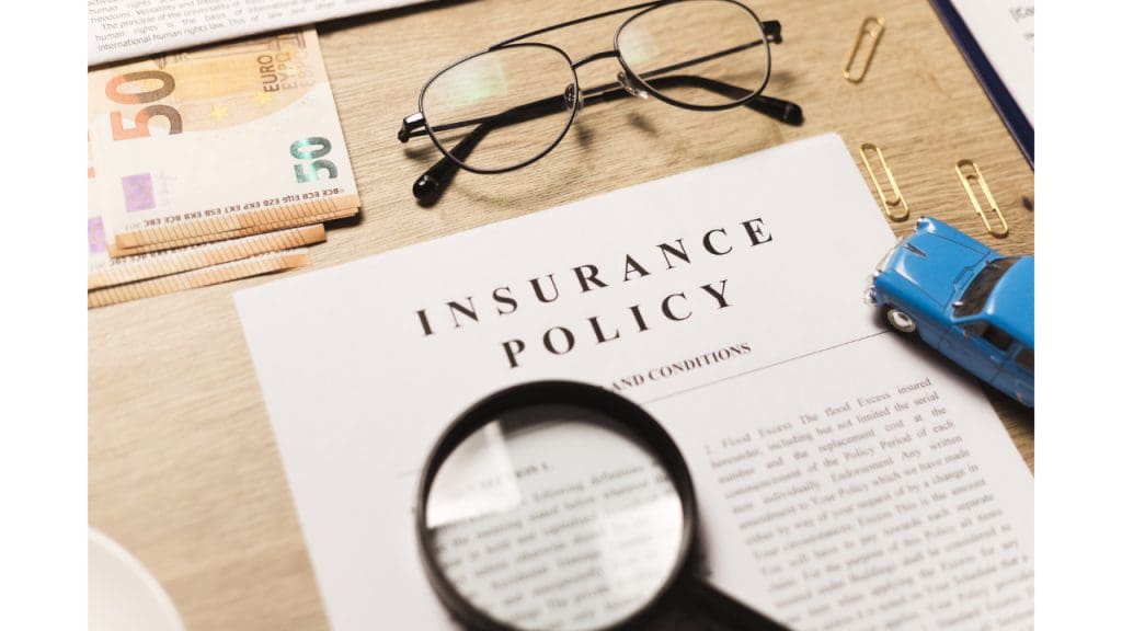 A close-up of an insurance policy document on a desk with a magnifying glass and glasses, suggesting a detailed review of the terms and conditions related to what is PIP for auto insurance, with a