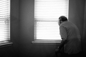 a man standing in front of a window looking out the window.