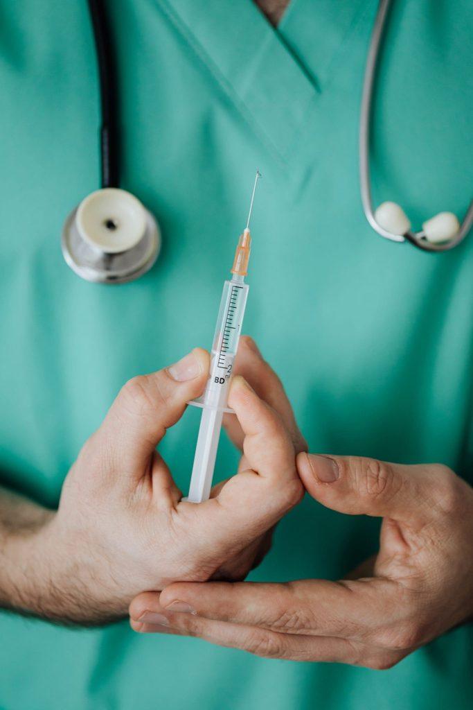 a person in a green scrub suit holding a needle.