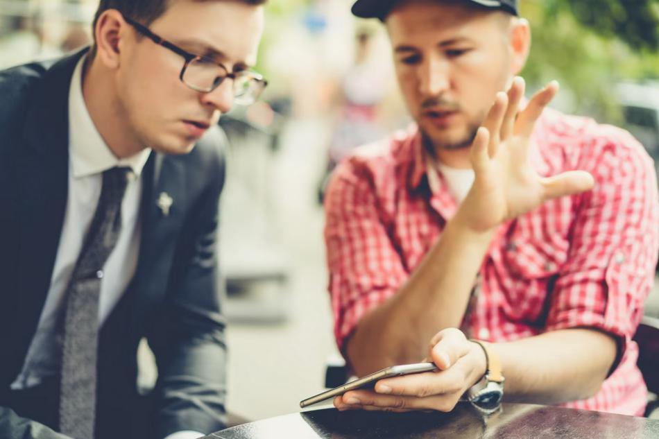 Two businessmen discussing an Uber and Lyft accident while looking at a cell phone.