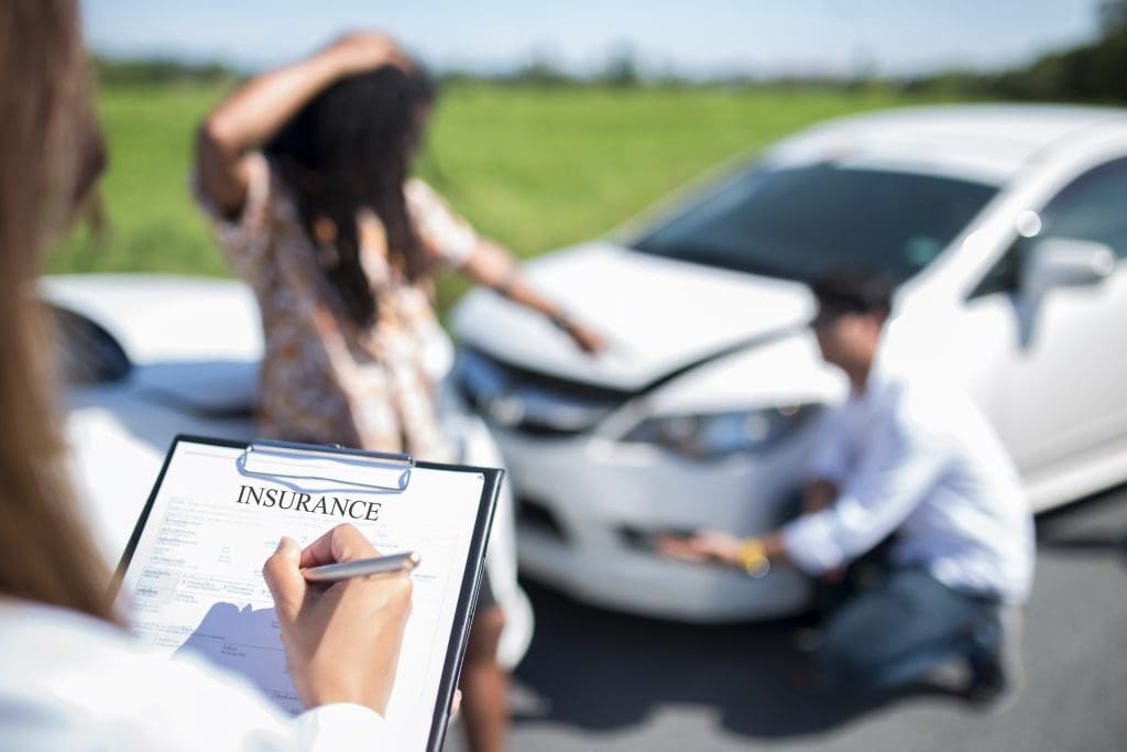 A woman holding a clipboard with a clipboard in front of a damaged car.
