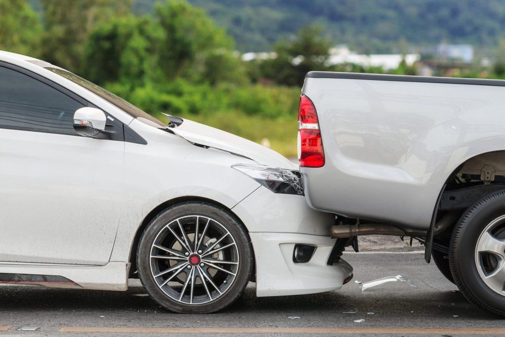 Rear-end collision between a white sedan and a silver pickup truck on a road.