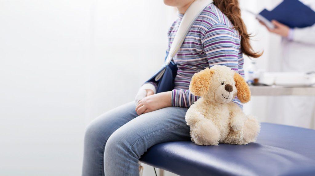 girl patient with broken arm waiting and in the background doctor looking at results