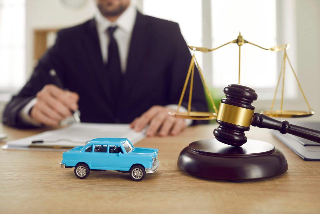 a blue toy car in front of a gavel and a well suited man at the back