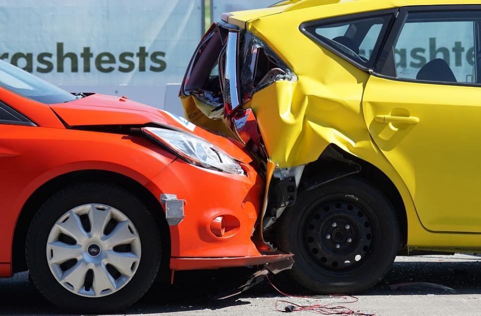 A red car and a yellow car after a rear-end collision. The front end of the red car is crumpled, and its hood is dented, while the rear of the yellow car is severely damaged. The word "crashtests" is visible in the background, highlighting potential uninsured motorist claims.