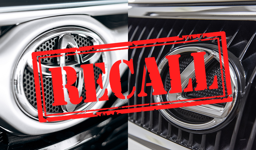 Close-up of two car grilles with a large "RECALL" stamp in red overlaid on the image. The left grille has a circular emblem, and the right grille has an angular design.