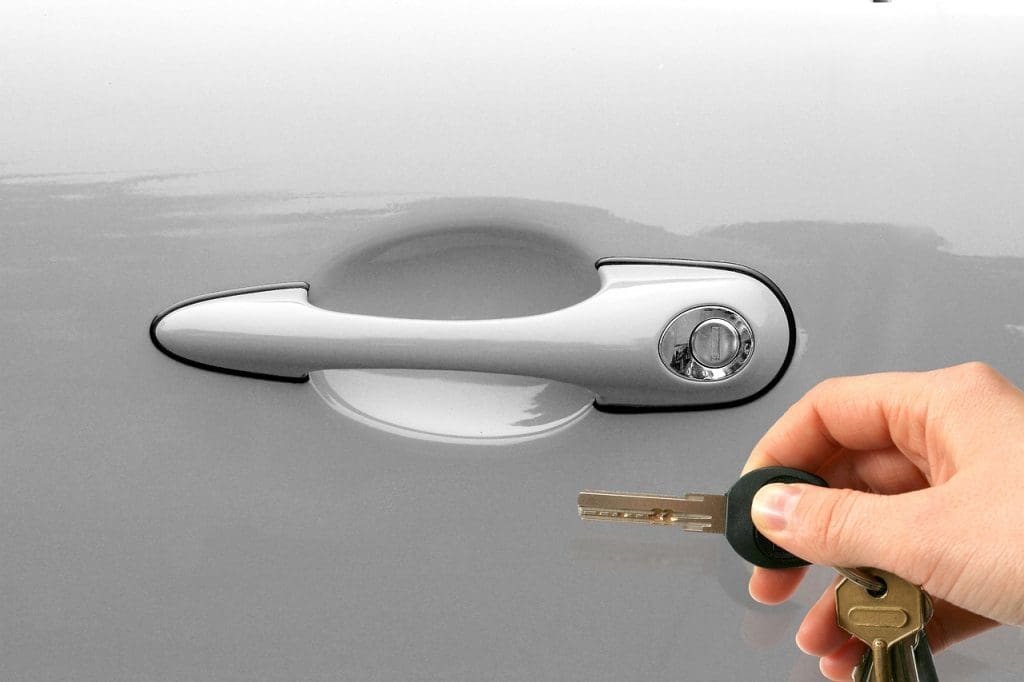 Hand holding car keys to a car door