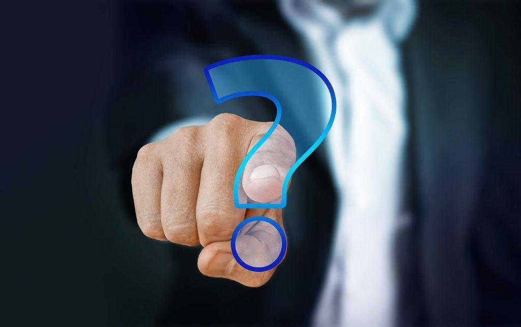 An attorney for a minor traffic accident, dressed in a suit, points directly at a transparent blue question mark in a digital representation, symbolizing inquiry or decision-making. The blurred background accentuates the focus on the hand and the question mark.