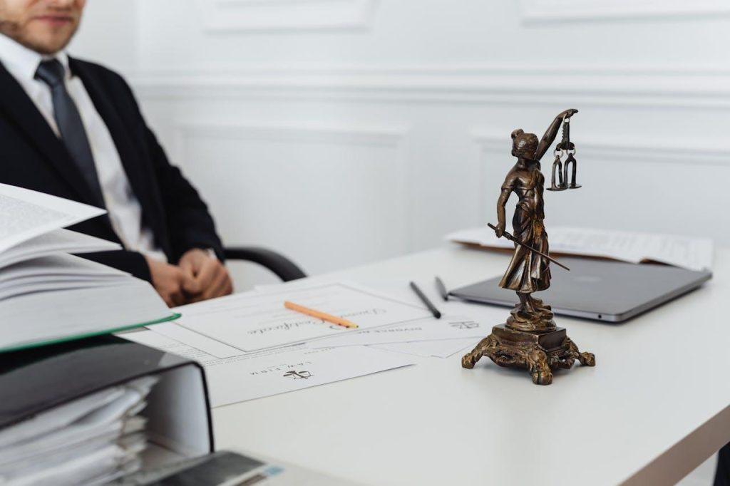 A person in a suit sits at a desk with documents related to pedestrian accidents, a laptop, and a small statue of Lady Justice. The scene suggests a legal or office setting focused on justice and advocacy for accident victims.