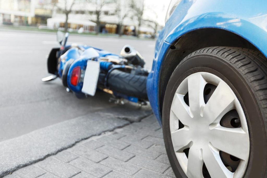 Motorcycle lying on the road next to a car tire after a collision, highlighting the severity of motorcycle accidents.