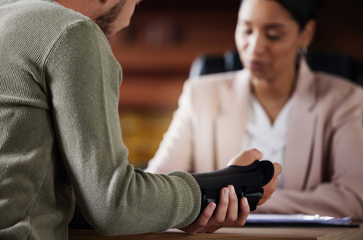 Injured person with wrist brace discussing car accident claim with a legal professional.
